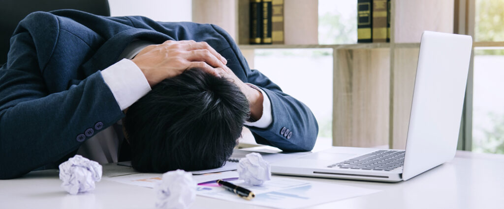 A frustrated person rests their head on a desk