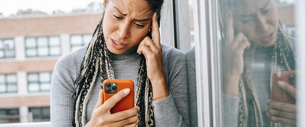 A woman looks at her smartphone with a look of concern on her face