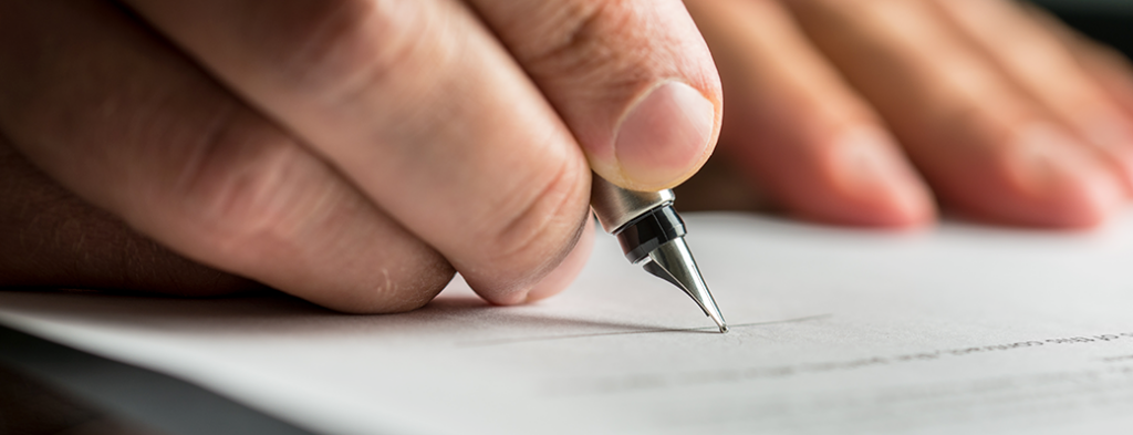 A person signs a document with a pen