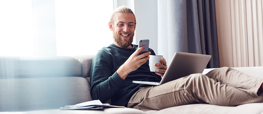User enjoying AI driven personalization on a laptop and phone while drinking a cup of coffee