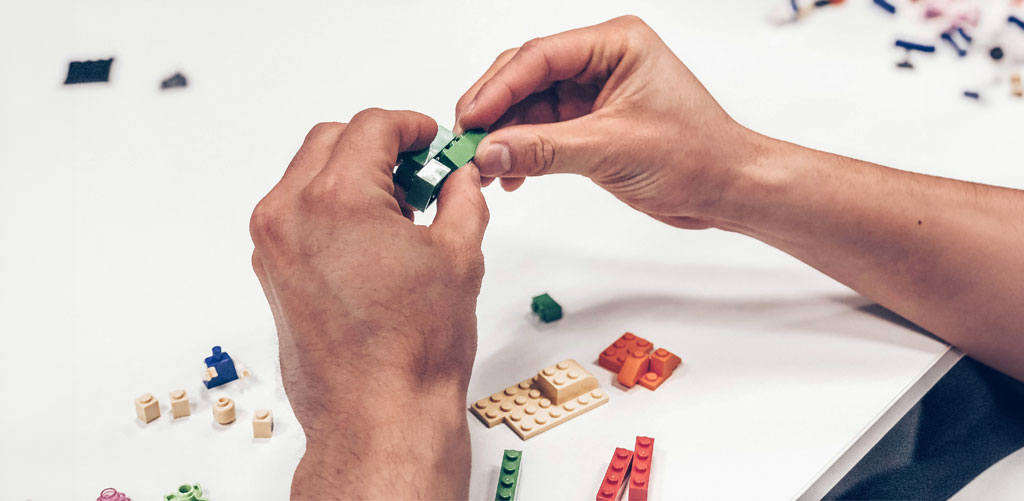 Hands assembling plastic building blocks to represent the shifts to make a CX investment compound