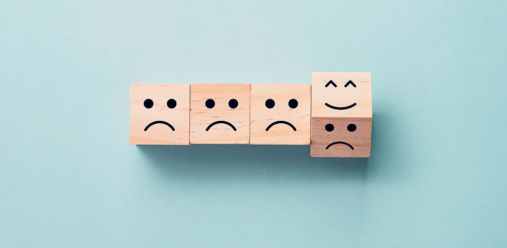 Wooden blocks showing sad faces with last block flipped to reveal a happy face to represent good user experience progress