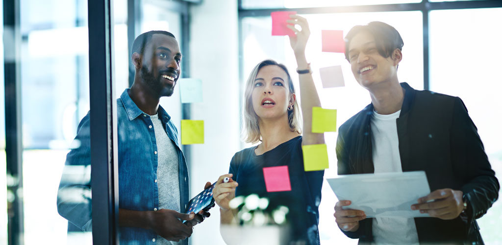 Three colleagues collaborating on data trust issues and placing sticky notes on glass wall